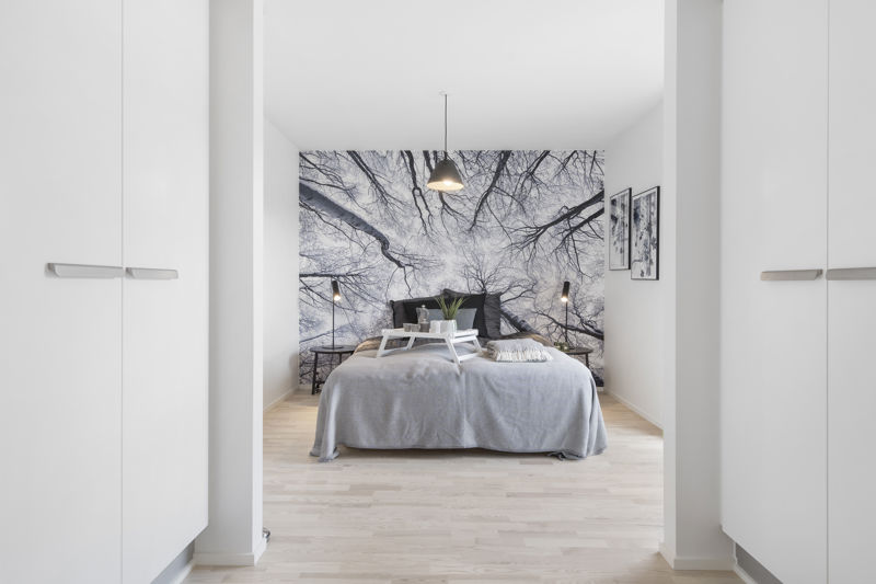 Soveværelse med hvide garderobeskabe i begge sider, lys seng, fototapet med trækroner, sengeborde, væglamper og pendel over sengen – inspiration til walk-in closet, soveværelsesindretning og nybyggeri med god skabsplads fra eurodan-huse.