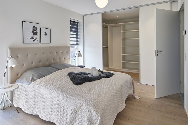 Soveværelse fra eurodan-huse med polstret sengegavl, lyse sengetekstiler, natbordslamper, vægkunst, åben dør til walk-in closet med hvide hylder og skydelåger – inspiration til nybyggeri med garderobe tæt på soveværelset og funktionelle husdrømme.
