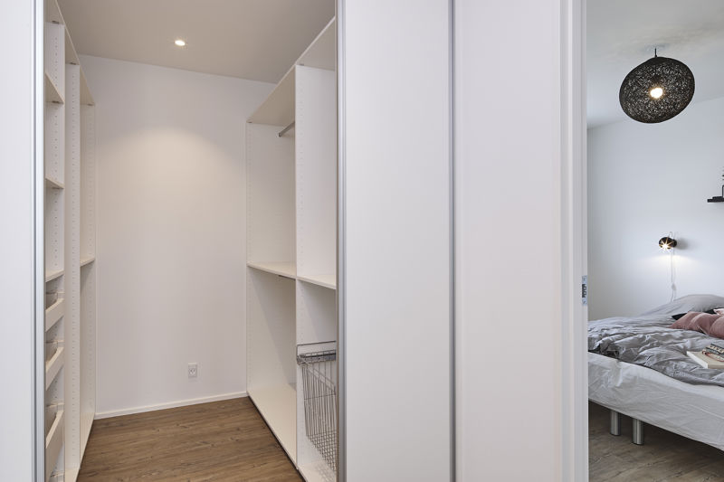 Walk-in closet med åbne hvide reoler, hylder, garderobestænger, trådkurve, indbygget spotlys og kig til soveværelse med rund sort pendel – inspiration til organiseret opbevaring, moderne husbyggeri og personlige husdrømme fra eurodan-huse.
