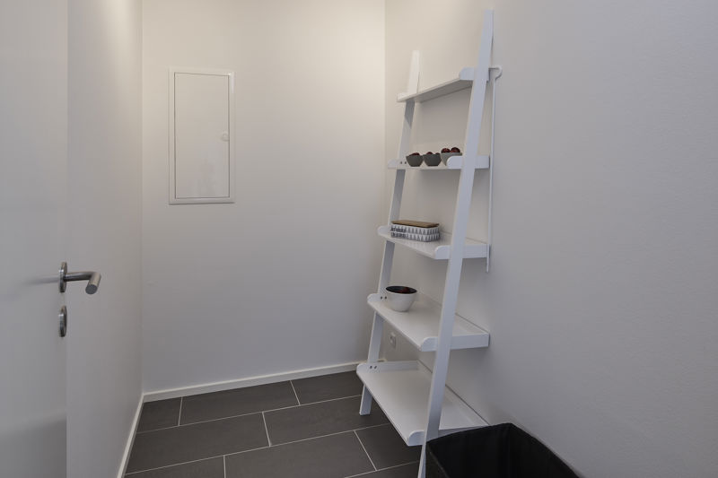 Lille depotrum fra eurodan-huse med grå klinkegulv, hvide vægge, hvid stigereol, indbygget vægskab og opbevaring af skåle og kurv på hylderne – inspiration til smart udnyttelse af plads i nybyggeri og moderne husbyggeri.