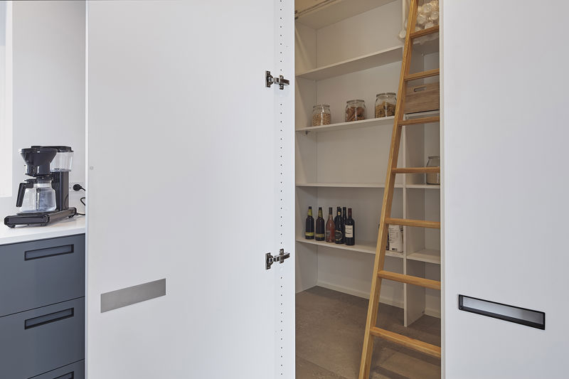 Depotrum fra eurodan-huse bag hvide skabslåger med åbne hylder, træstige, opbevaringsglas, vinflasker og kaffemaskine synlig ved køkkenbordet – inspiration til skjult depot, praktisk nybyggeri og husbyggeri med god opbevaringsplads.
