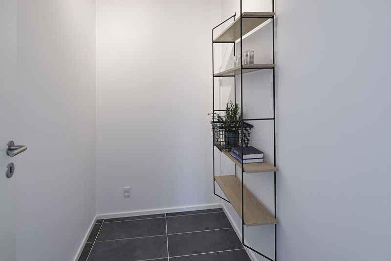 Depotrum fra eurodan-huse med sort metalreol, lyse træhylder, grå klinkegulv, hvid væg, plantekurv og bøger på hylderne – inspiration til enkel og funktionel opbevaring i nybyggeri, husbyggeri og personlige husdrømme.
