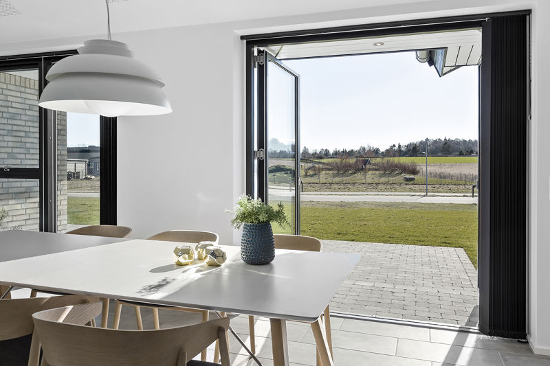 Lyst køkkenalrum i moderne nybyggeri fra eurodan-huse med stort spisebord, sorte vinduesrammer og brede foldedøre, der åbner direkte ud til terrasse og have.