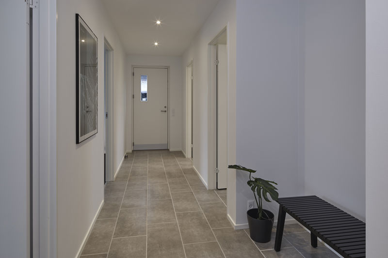 Entré og gang fra eurodan-huse med grå klinkegulv, sort bænk, grøn plante i sort krukke, indbyggede spots, vægbillede og hoveddør med smalt glasfelt – inspiration til praktisk indgang i nybyggeri og moderne husdrømme.