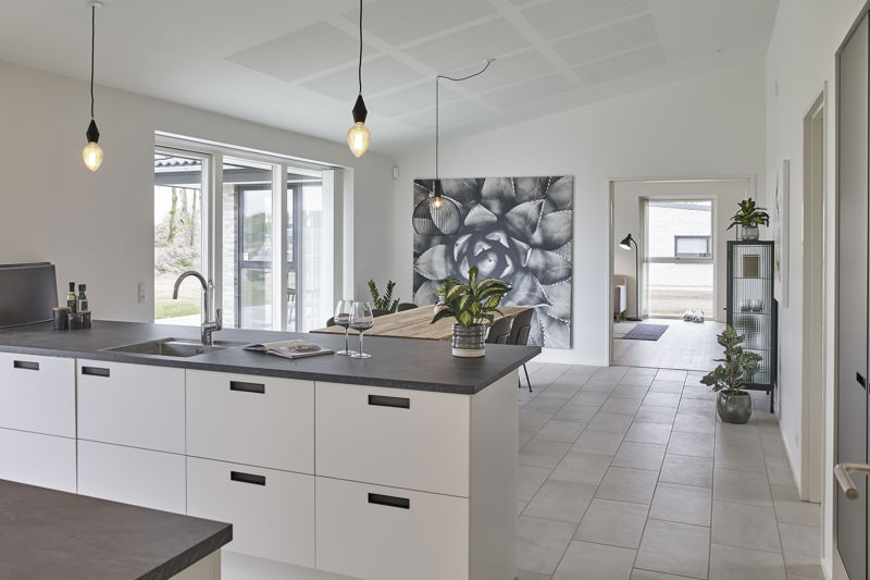 Køkken-alrum fra eurodan-huse set fra køkkenøen med hvide skuffer, mørk bordplade, vask og armatur, pendler med synlige pærer, stort sort-hvidt blomstermotiv på væggen og kig gennem alrummet – inspiration til moderne nybyggeri og personlige husdrømme.