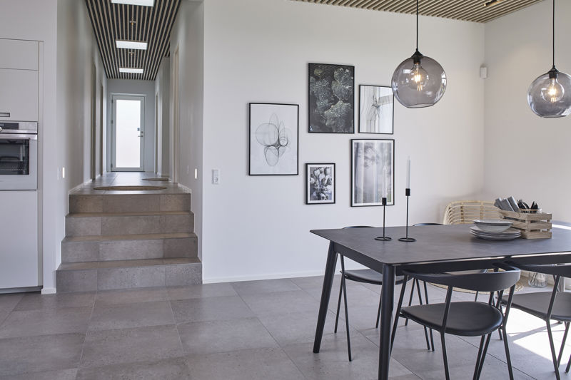Køkken fra eurodan-huse med lyse beige skabsfronter fra gulv til loft, integreret sort ovn i højskab, åben skabslåge ind til depot/opbevaring, sort vask og armatur på køkkenøen samt lyst sildebensgulv – konkret inspiration til funktionelt nybyggeri, husbyggeri og gennemtænkte husdrømme.