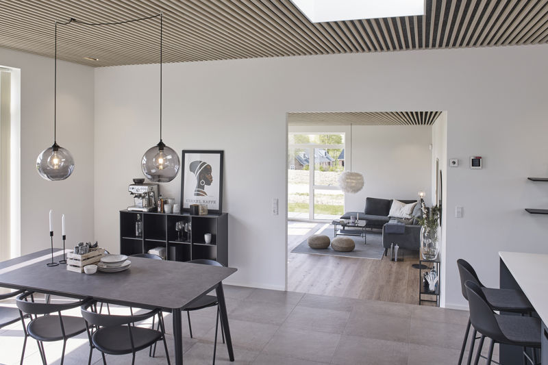 Detalje af moderne køkkenløsning fra eurodan-huse med sammenhængende skabsvæg, skjult depot bag høj skabslåge, integreret ovn, beige køkkenfronter, hvide bordplader og sort armatur ved køkkenøen – inspiration til praktisk opbevaring i nybyggeri og moderne husdrømme.