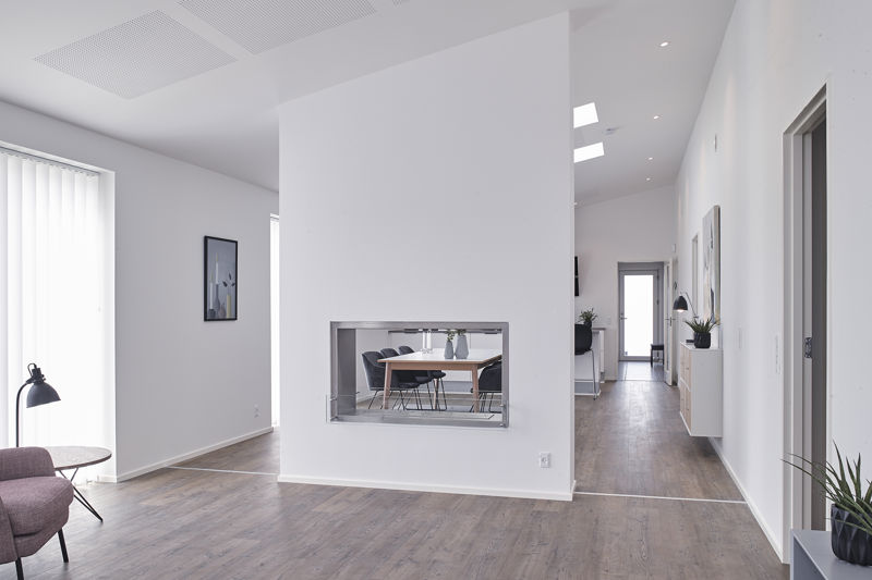 Åbent opholdsrum fra eurodan-huse med kig fra stue mod spiseplads gennem lavt indbygget vindue i væggen, rosa lænestol i venstre side, højt loft, lyse vægge og lang gang med ovenlys – inspiration til gennemtænkt nybyggeri, husbyggeri og kreative husdrømme.