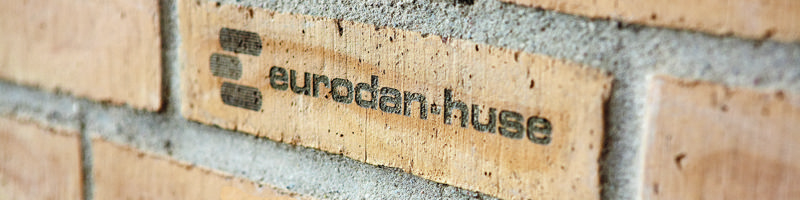 Nærbillede af eurodan-huse-logo præget i en lys mursten på facaden af et nybygget hus.
