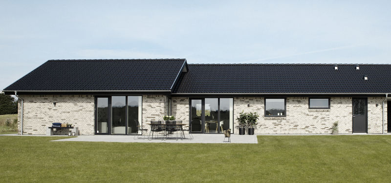 Nybygget længehus med lys murstensfacade, mørkt tegltag, store vinduespartier, terrasse og grøn græsplæne.