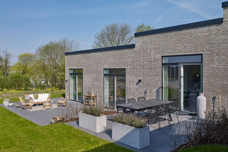 Terrassemiljø fra eurodan-huse med to opholdszoner, spisebord med mørke havestole, loungeområde med lyse møbler, plantekasser, store vinduer og lys murstensfacade mod grøn have – inspiration til nybyggeri med fleksibelt uderum og husdrømme.