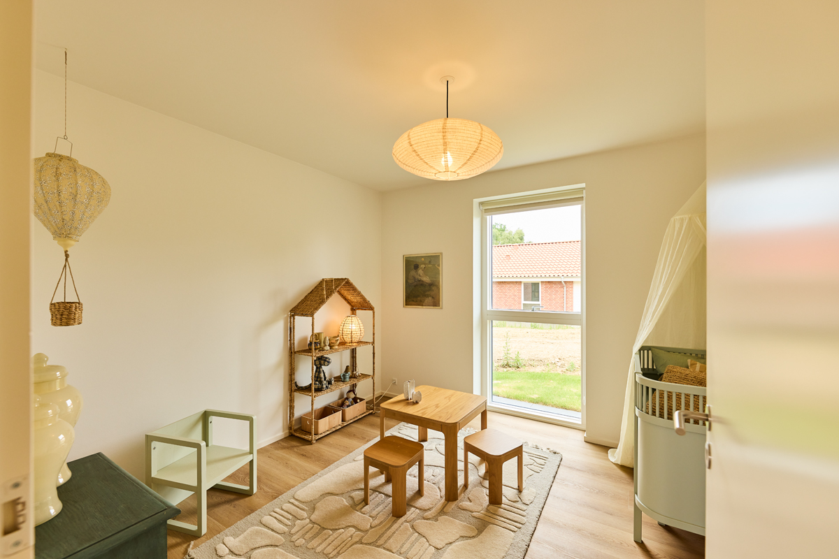 Børneværelse fra eurodan-huse med lille bord og stole, børnesen, legetæppe, reol og højt vindue – inspiration til familievenligt nybyggeri.