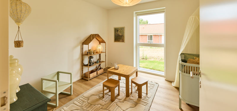 Børneværelse fra eurodan-huse med lille bord og stole, børnesen, legetæppe, reol og højt vindue – inspiration til familievenligt nybyggeri.