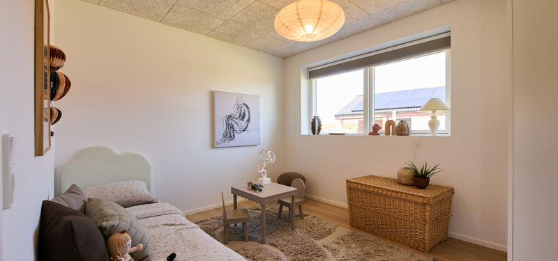 Børneværelse fra eurodan-huse med lav seng, lille legebord, flettet opbevaringskiste og stort vindue – inspiration til nybyggeri med kreative børneværelser og husdrømme.