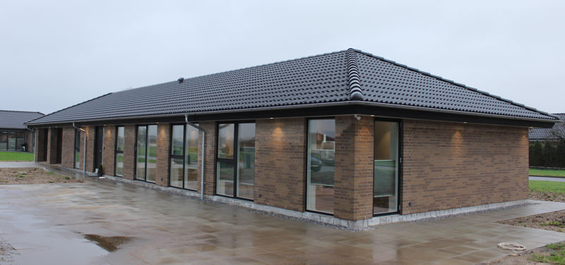 Moderne nybygget drømmehus fra eurodan-huse i brune mursten med sort valmtag, store gulv-til-loft vinduespartier og en lang, enkel facade med fokus på lys og moderne arkitektur.