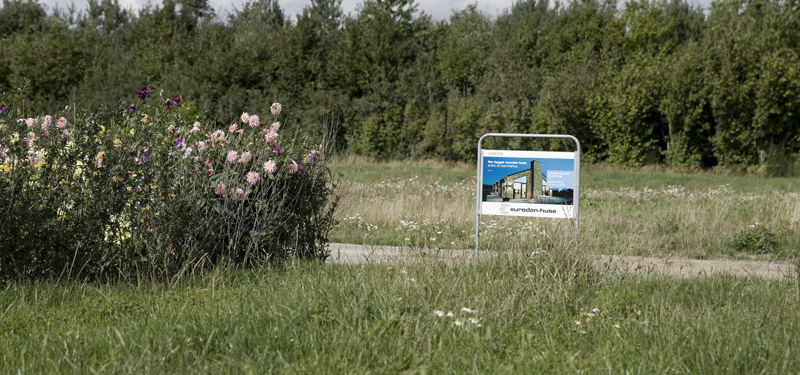 Grøn byggegrund med blomster, træer og skilt fra eurodan-huse – klar til nybyggeri og et nyt drømmehus.