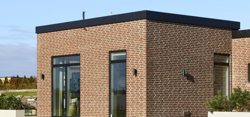 Detalje af nybygget funkishus med rødbrun teglfacade, sorte vinduesrammer og moderne arkitektur fra eurodan-huse
