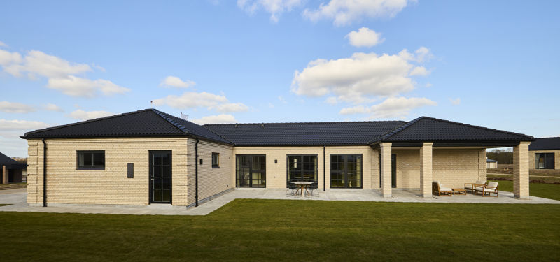 Palæinspireret facade fra eurodan-huse med lyse mursten, sort tegltag, symmetriske vinduespartier, sort dør, overdækket terrasse og søjlelignende murdetaljer – inspiration til elegant nybyggeri og klassiske husdrømme.
