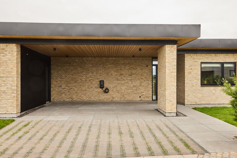 Carport fra eurodan-huse med lyse murstenssøjler, sort loftkant, træbeklædt underside, indbygget ladestander og direkte adgang mod boligen – inspiration til praktisk nybyggeri med carport, garage og moderne husbyggeri.