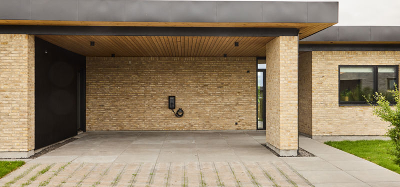 Carport fra eurodan-huse med lyse murstenssøjler, sort loftkant, træbeklædt underside, indbygget ladestander og direkte adgang mod boligen – inspiration til praktisk nybyggeri med carport, garage og moderne husbyggeri.