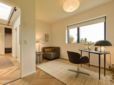 Gæsteværelse fra eurodan-huse med lille hyggekrog, lænestol, skrivebord, sort bordlampe, stort vindue, tæppe – inspiration til fleksible rum i nybygget hus og gennemtænkt husbyggeri.