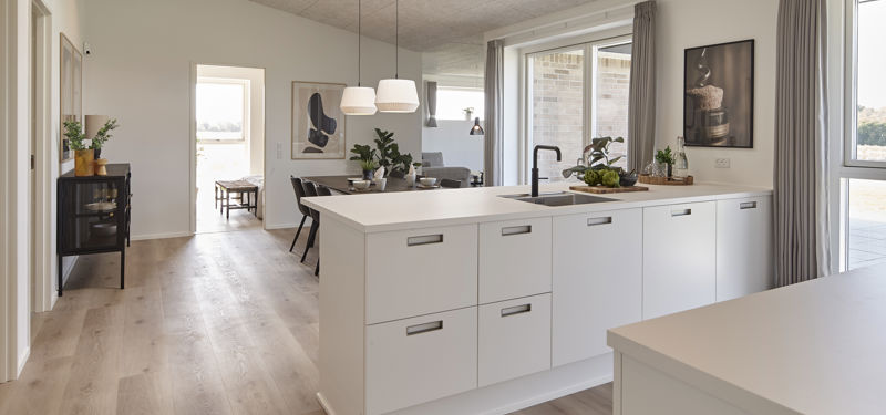 Lyst køkken-alrum fra eurodan-huse med hvidt køkken, trædetaljer, spisebord med stole, store vinduer, åben planløsning og plads til både madlavning og samvær – inspiration til nybyggeri, husbyggeri og indretning af et moderne nybygget hus.
