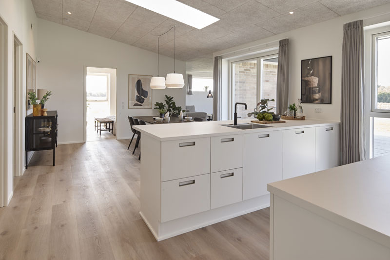 Lyst køkken-alrum fra eurodan-huse med hvidt køkken, trædetaljer, spisebord med stole, store vinduer, åben planløsning og plads til både madlavning og samvær – inspiration til nybyggeri, husbyggeri og indretning af et moderne nybygget hus.