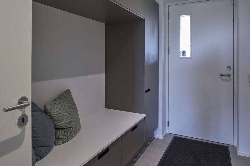 Entré fra eurodan-huse med indbygget bænk i garderobeskab, mørke skabsfronter, hvide hylder, puder på siddepladsen, grå gulvfliser og hoveddør med smalt vindue – inspiration til nybyggeri og husdrømme med praktisk opbevaringsløsning.