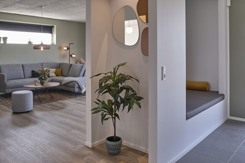 Opholdsrum fra eurodan-huse med grå sofa, runde sofaborde, plante i krukke, spejle på væggen og indbygget alkove med grå siddehynde og gul pude ved siden af stuen – inspiration til nybyggeri og husdrømme med ekstra siddeplads.