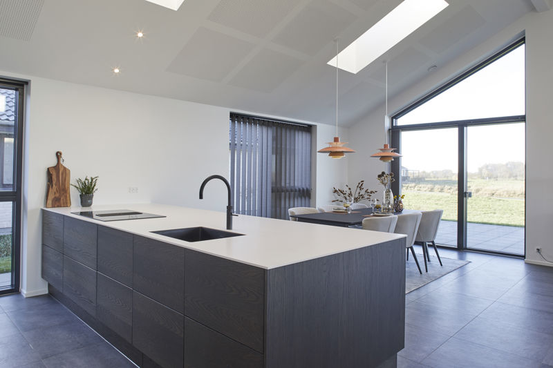 Moderne køkken-alrum fra eurodan-huse med mørk køkkenø, hvid bordplade, sort vask og armatur, integreret kogeplade, spiseplads ved store vinduer, mørke gulvfliser og loft med ovenlys – inspiration til funktionelt nybyggeri og stilrene husdrømme.
