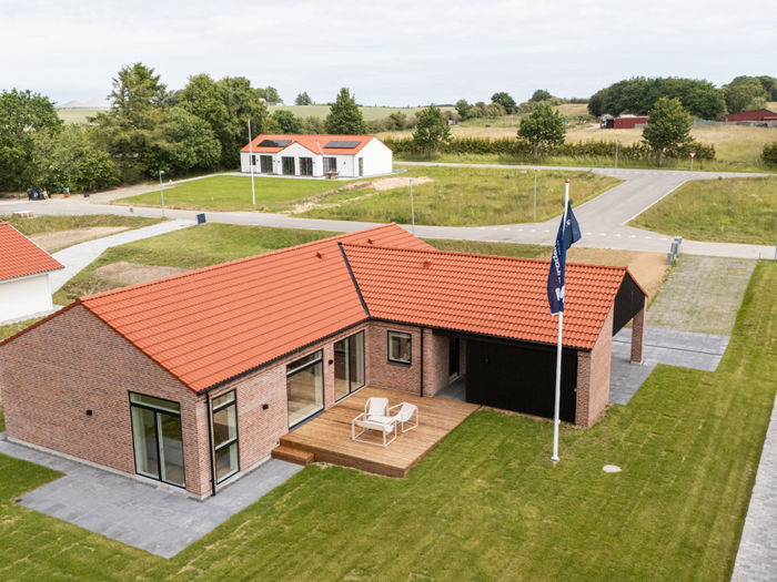 Luftfoto af vinkelhus fra eurodan-huse med rødt tegltag, muret facade, stor træterrasse, have og indkørsel – inspiration til nybyggeri, husbyggeri og moderne husdrømme.