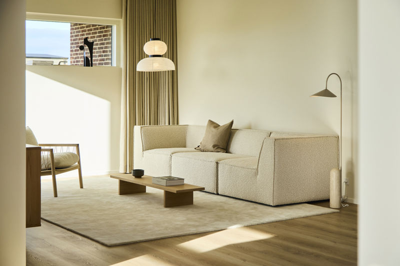 Lys stue fra eurodan-huse med blød hvid modulsofa, lavt træbord, lang beige gardinvæg, høj standerlampe og lille siddeplads ved vinduet – inspiration til moderne nybyggeri, indretning af stue og lyse husdrømme.