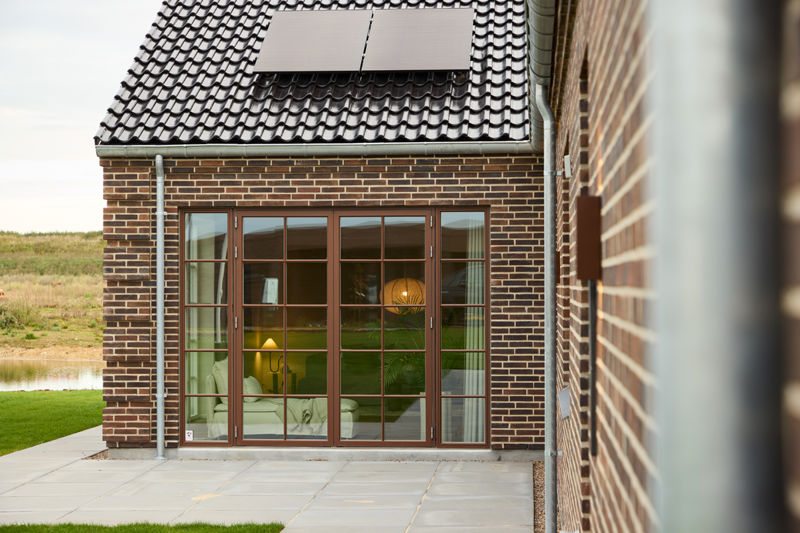 Flisebelagt terrasse i vinklen på et hus i palæstil med store sprossede vinduer
