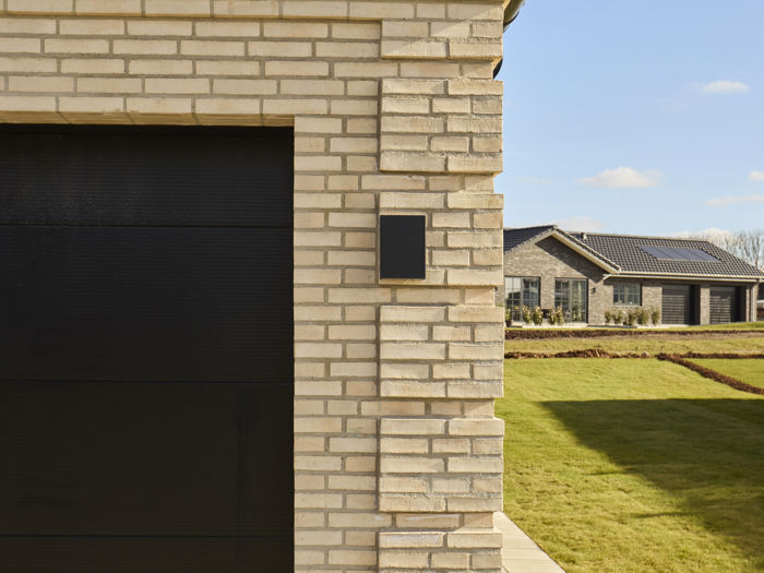 Detalje af husbyggeri med lys murstensfacade, sort garageport og sort tegltag