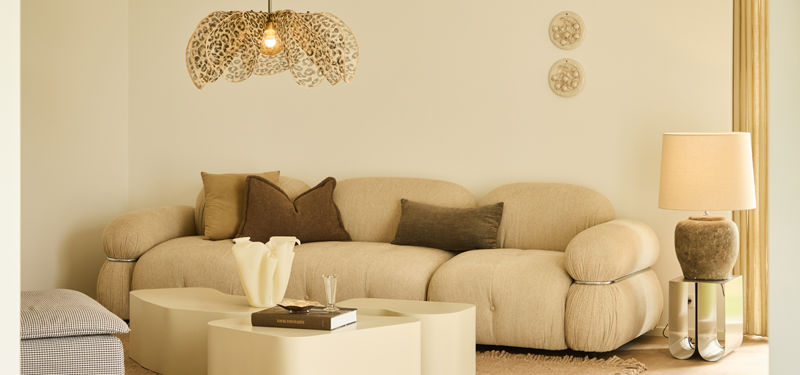Lys stue fra eurodan-huse med beige modulsofa, firkantet sofabord, stort gulvtæppe, dekorativ pendellampe og gulvlampe ved gardinerne – inspiration til rolig boligindretning, moderne nybyggeri og husdrømme.