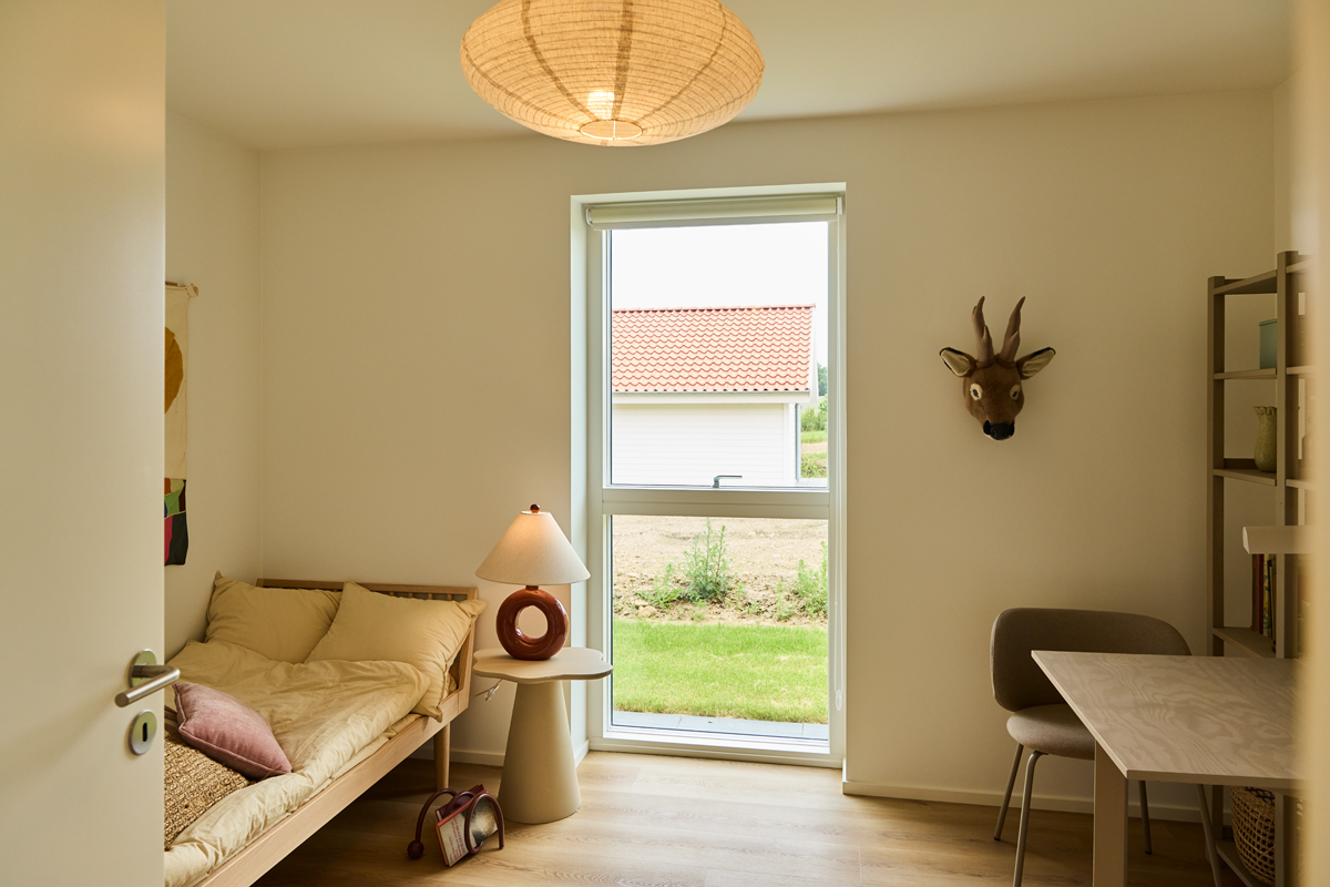 Gæsteværelse fra eurodan-huse med daybed, lille sidebord, skriveplads, reol, stort vindue og vægdekoration – inspiration til multifunktionelle rum i nybyggeri.