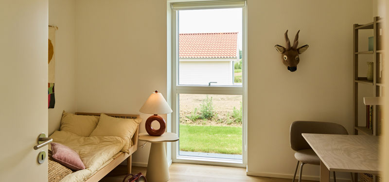 Gæsteværelse fra eurodan-huse med daybed, lille sidebord, skriveplads, reol, stort vindue og vægdekoration – inspiration til multifunktionelle rum i nybyggeri.