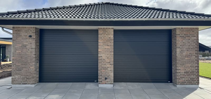 Husbyggeri med dobbeltgarage, sort tegltag og moderne murstensfacade