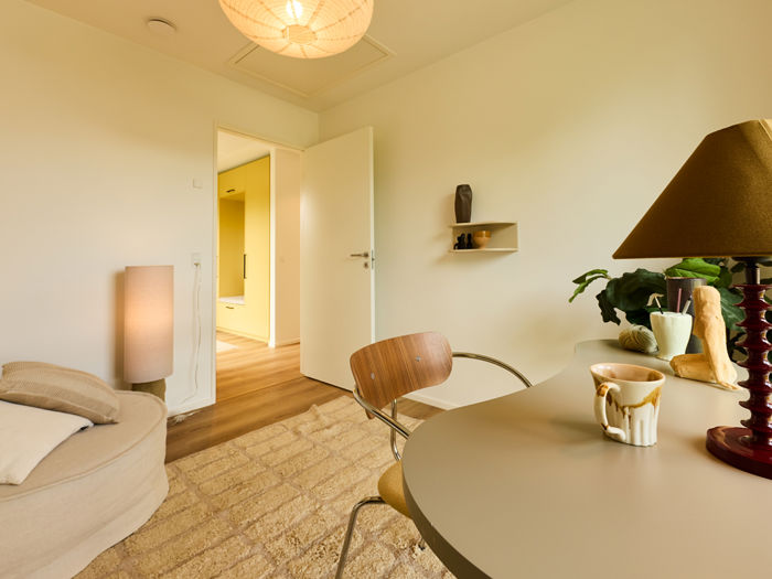 Kontor fra eurodan-huse med rundt skrivebord, designstol, bordlampe, åben dør til gang og kig mod gul skabsvæg – inspiration til fleksibelt nybyggeri.