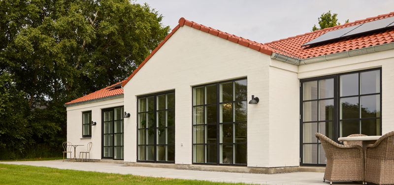 Facade fra eurodan-huse med hvide mursten, rødt tegltag, sorte vinduer med sprosser, udendørslamper og terrasse med loungemøbler – inspiration til nybyggeri i palæstil.