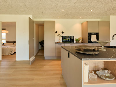 Køkken fra eurodan-huse med beige skabsvæg, integreret ovn, mørk bordplade, stor køkkenø og åben låge ind til depot/opbevaring – inspiration til funktionelt nybyggeri og gennemtænkte husdrømme.