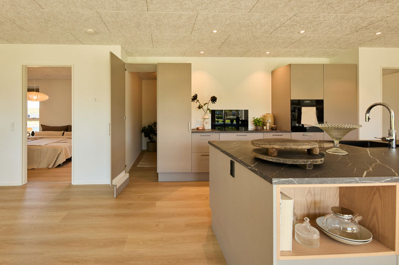 Køkken fra eurodan-huse med beige skabsvæg, integreret ovn, mørk bordplade, stor køkkenø og åben låge ind til depot/opbevaring – inspiration til funktionelt nybyggeri og gennemtænkte husdrømme.