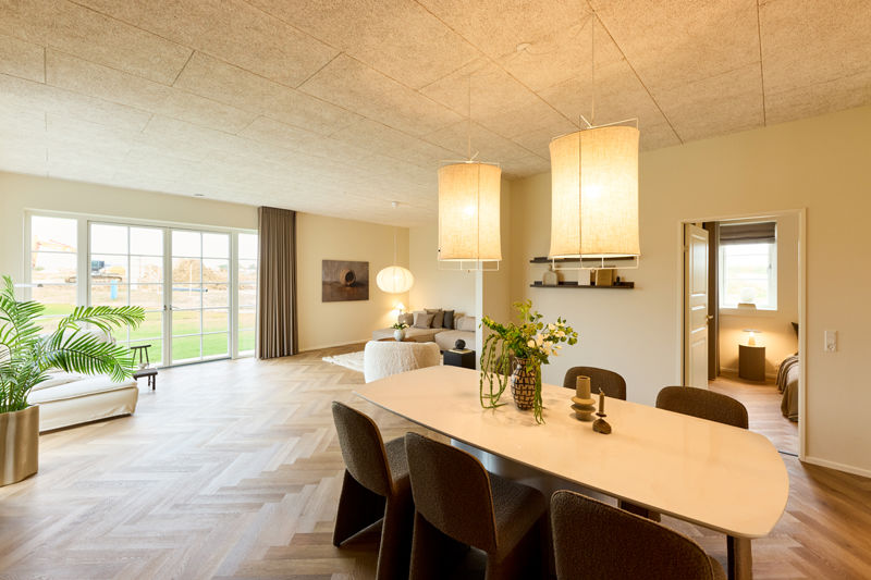 Lyst køkken-alrum med langbord og åben forbindelse til stuen i et nyt hus