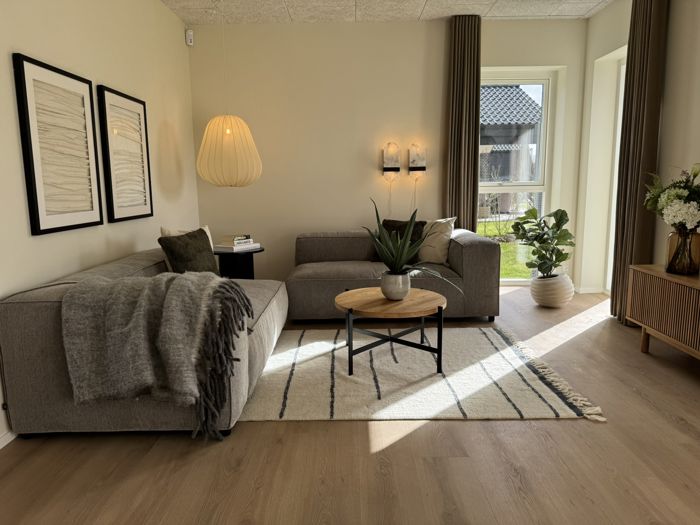 Stue i nybyggeri med sofahjørne, store vinduer og varm nordisk indretning
