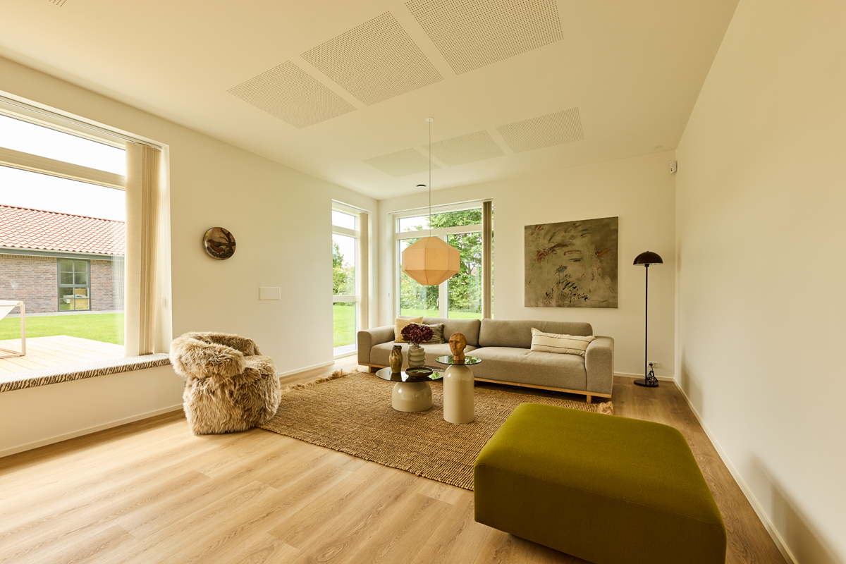 Stue fra eurodan-huse med sansevindue, lys sofa, grønt puf, rundt sofabord, gulvtæppe, pendellampe og store vinduer – inspiration til indretning i moderne nybyggeri.
