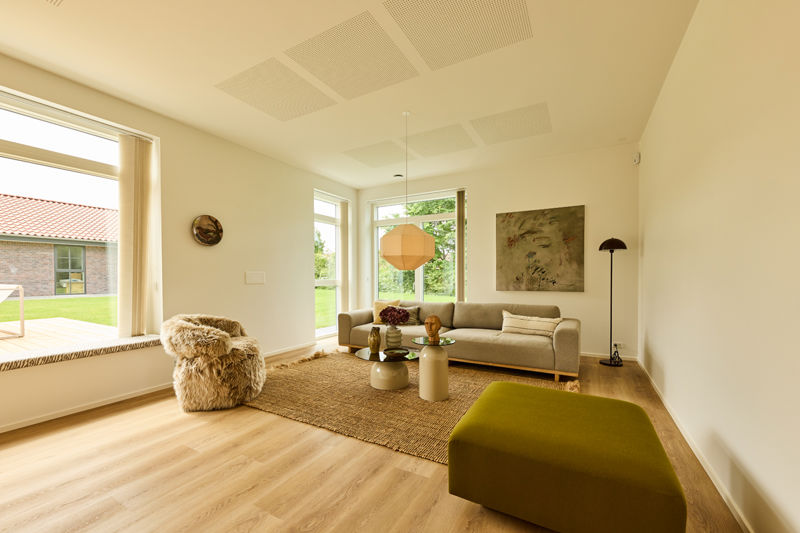 Stue fra eurodan-huse med sansevindue, lys sofa, grønt puf, rundt sofabord, gulvtæppe, pendellampe og store vinduer – inspiration til indretning i moderne nybyggeri.