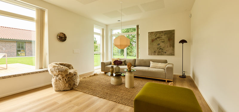 Stue fra eurodan-huse med sansevindue, lys sofa, grønt puf, rundt sofabord, gulvtæppe, pendellampe og store vinduer – inspiration til indretning i moderne nybyggeri.