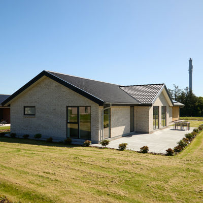 Hus fra eurodan-huse set udefra med lyse mursten, mørkt tegltag, sorte vinduer, stor terrasse og grøn have – inspiration til nybyggeri, familievilla og moderne husdrømme.