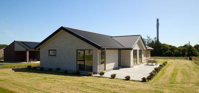Hus fra eurodan-huse set udefra med lyse mursten, mørkt tegltag, sorte vinduer, stor terrasse og grøn have – inspiration til nybyggeri, familievilla og moderne husdrømme.