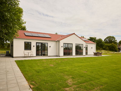 Hvid facade i palæstil fra eurodan-huse med rødt tegltag, sorte sprossevinduer, solceller, fliseterrasse og grøn græsplæne – inspiration til klassisk nybyggeri og husdrømme.